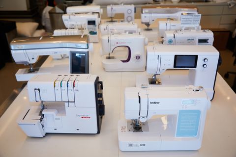 over a dozen different sewing machines and sergers on a white table as part of good housekeeping's best sewing machines testing