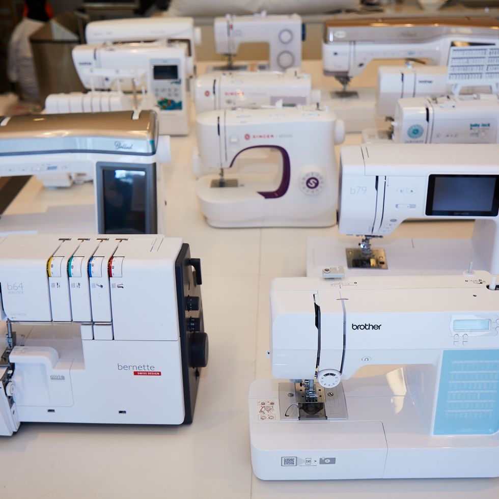 a variety of sewing machines set up on a white table facing the camera as part of good housekeeping's sewing machine testing to find the best sewing machines for beginners