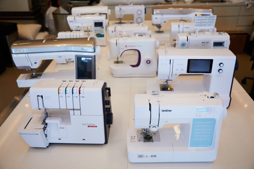 a variety of sewing machines set up on a white table facing the camera as part of good housekeeping's sewing machine testing to find the best sewing machines for quilting