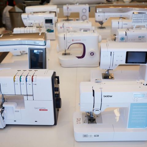 a dozen different sewing machines and sergers on a table in the textiles lab as part of serger testing