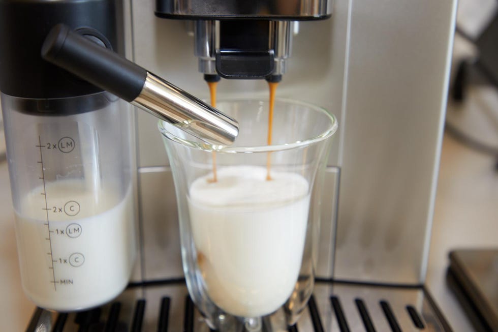 espresso machine producing coffee into a glass with frothed milk