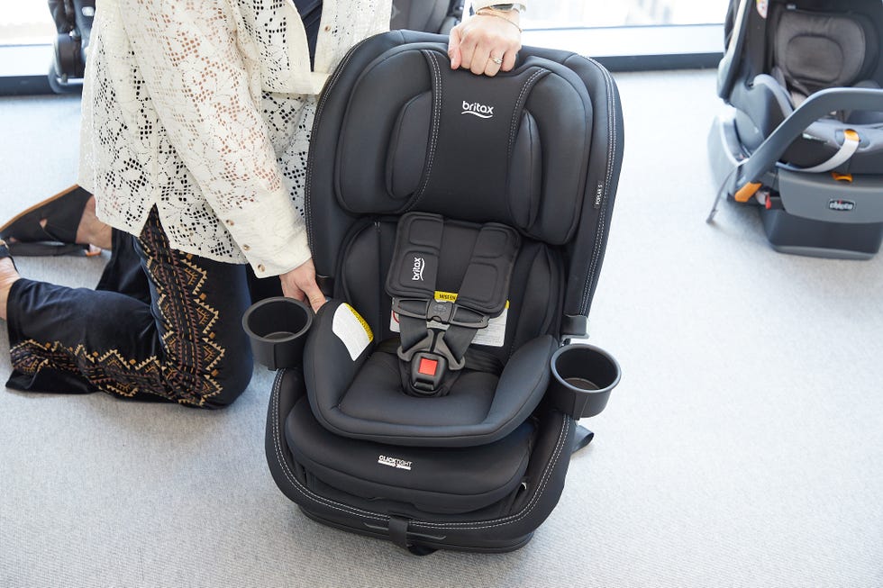 a person in a white shirt and black pants lifts the headrest of the britax poplar car seat