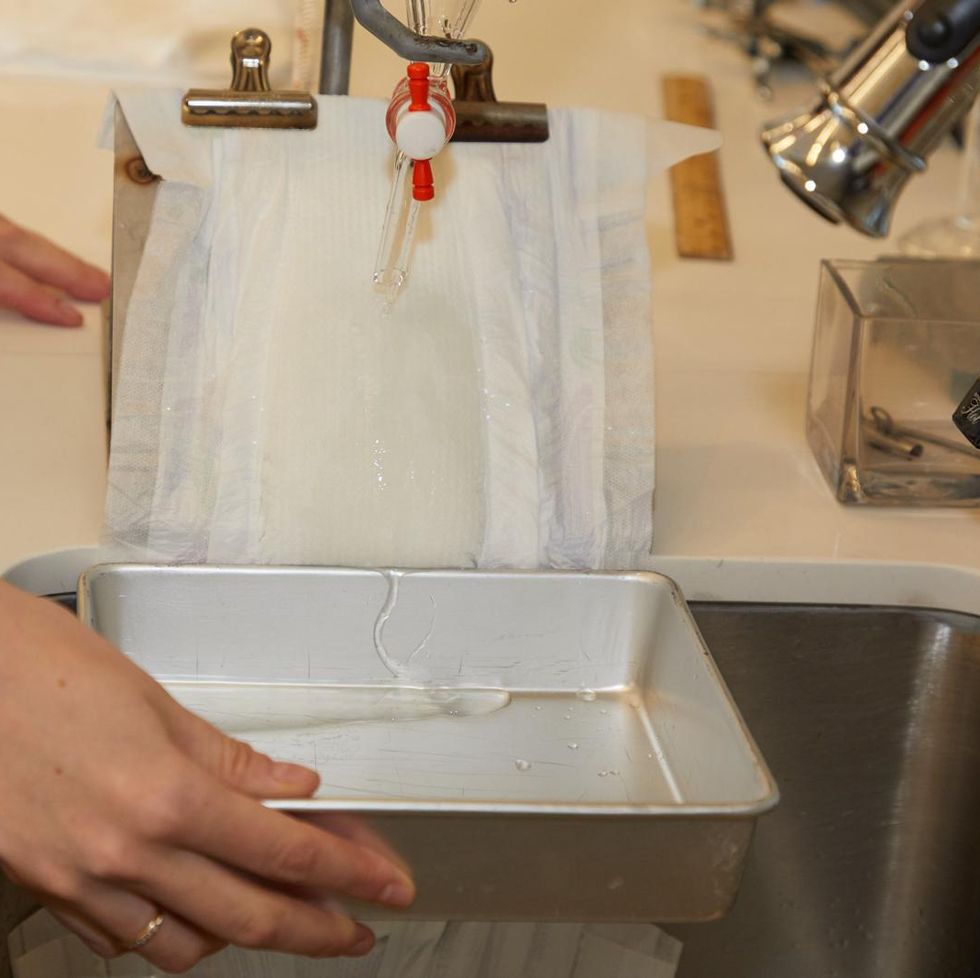 a gh analyst holding a metal tray at the bottom of a diaper that's mounted at a 45 degree angle during absorbency tests