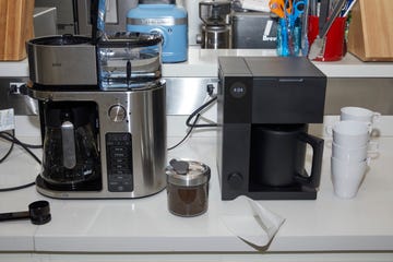 two coffee makers on a white countertop with coffee mugs and grounds beside the machines