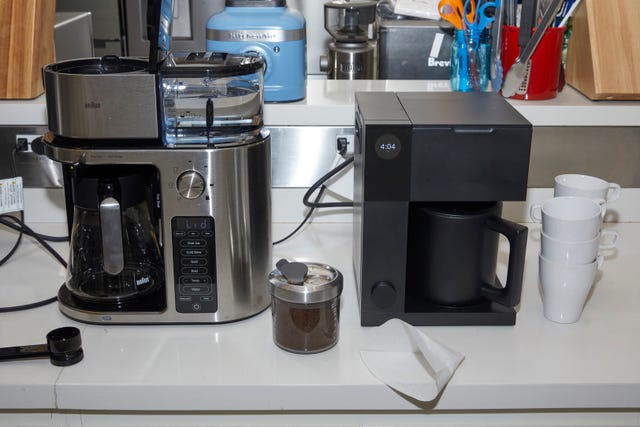 two coffee makers on a white countertop with coffee mugs and grounds beside the machines