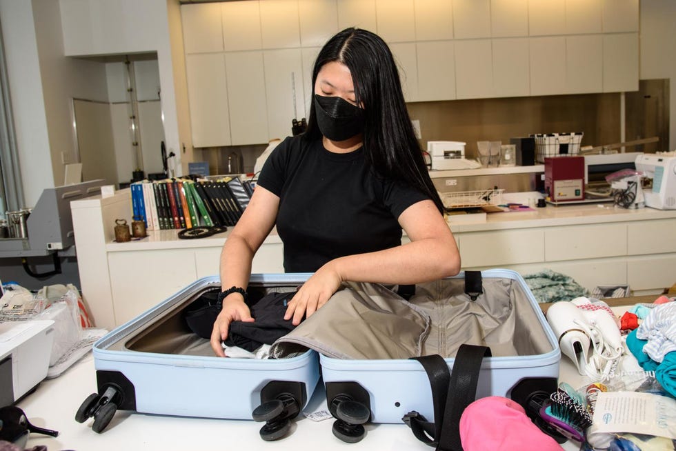 a woman packs a light blue suitcase