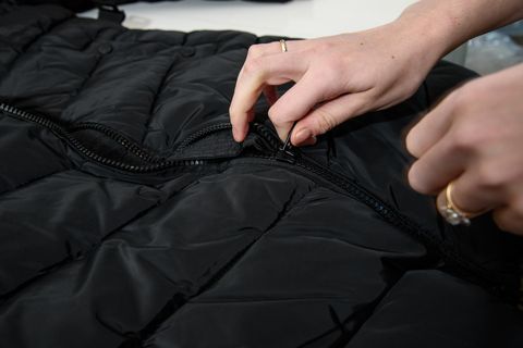 a close up of hands pulling a zipper on a black puffy winter coat, part of good housekeeping's construction test to find the best winter coat