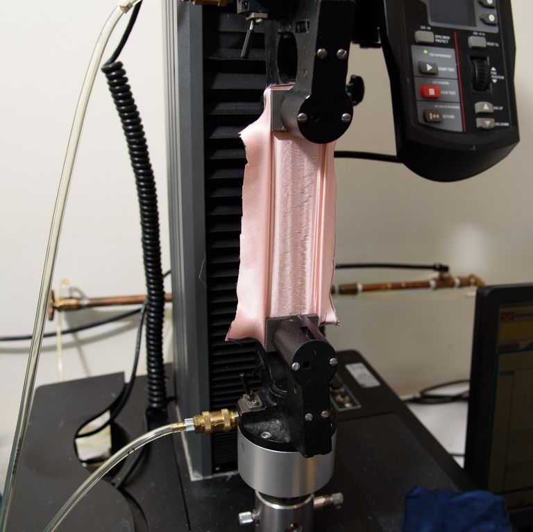 a specialized machine called the instron pulling a swatch of pink silk fabric to measure the force needed to break the swatch, strength testing