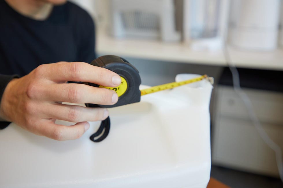 a hand holds a retractable tape measure, with the yellow measuring tape extended towards a humidifier on a table