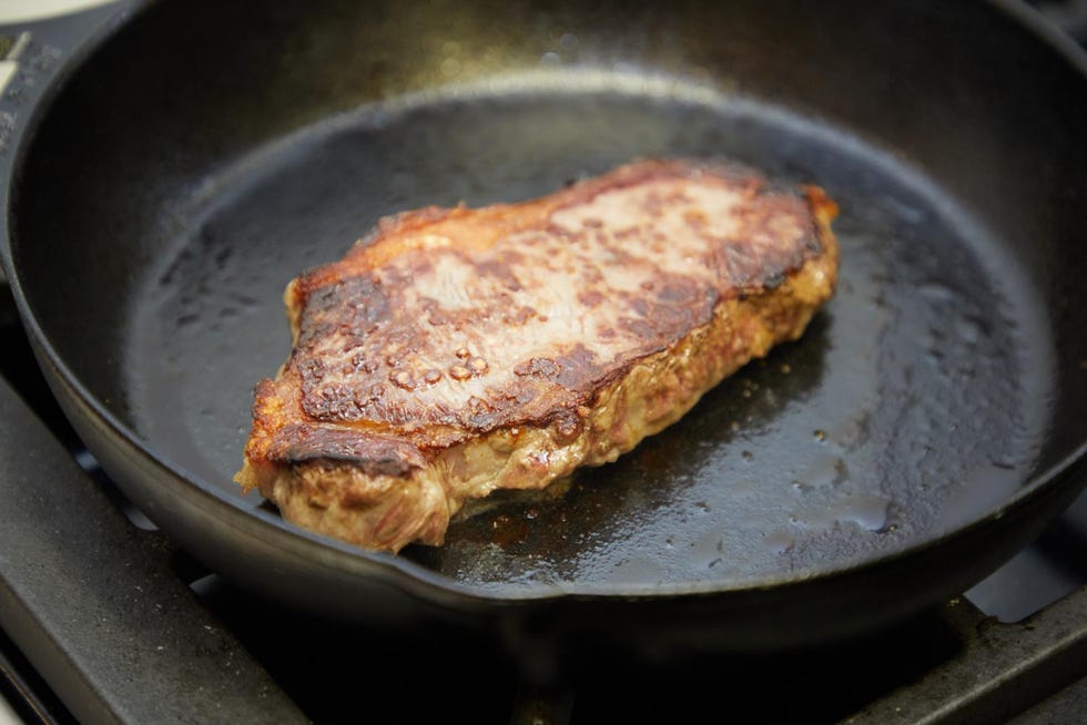 a seared steak cooking in a cast iron skillet