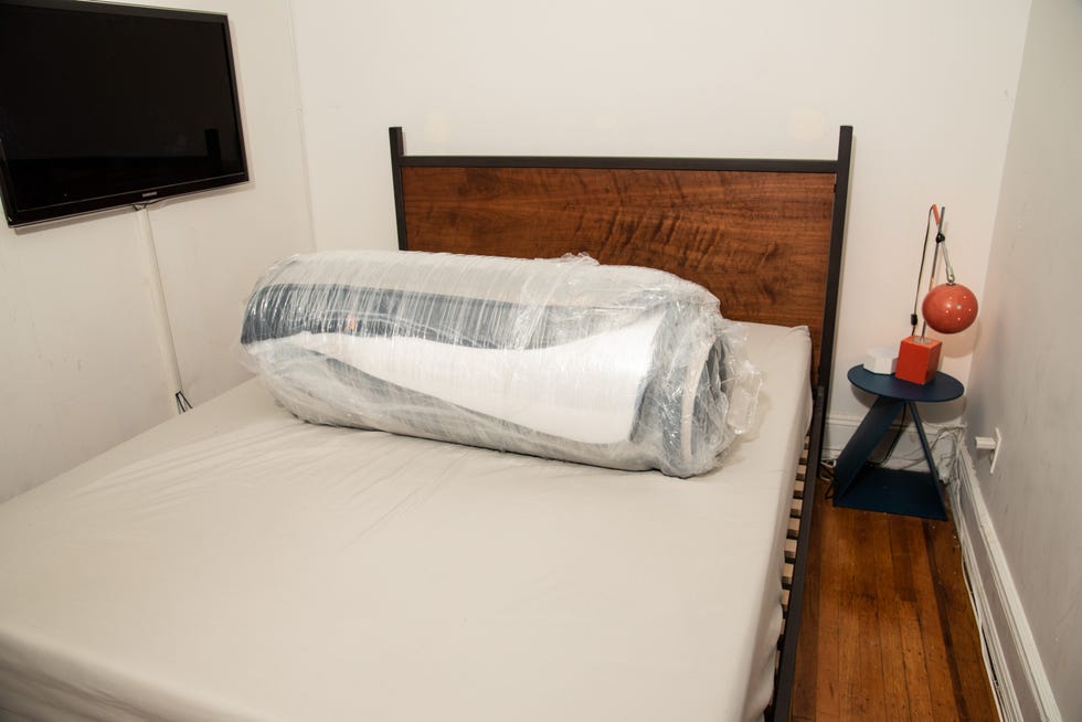 a compressed, rolled up mattress wrapped in plastic on a bed base