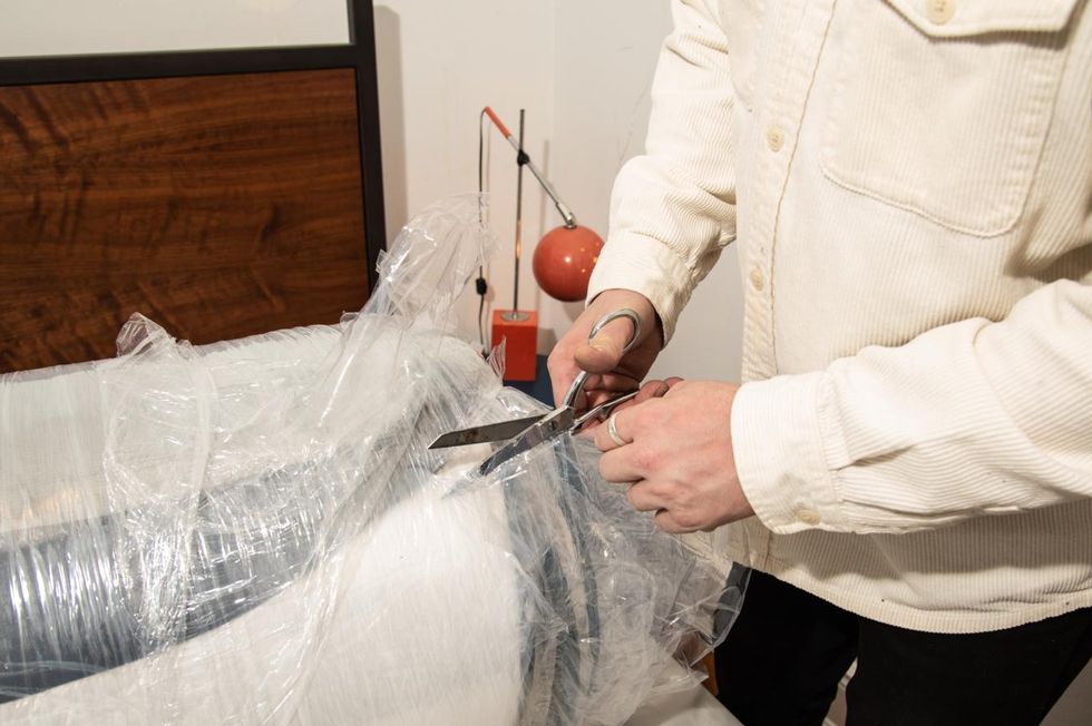a person cuts open a rolled up and compressed mattress