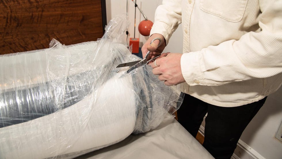 how to shop for a mattress - delivery and unboxing a person cuts open a rolled up and compressed mattress