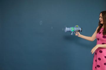 a person holding a toy fart blaster against a blue wall