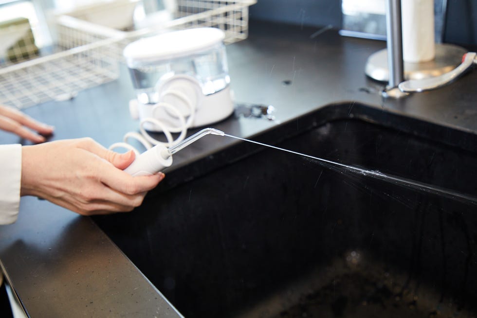 a person holding a water flosser wand as it sprays a strong jet of water into a sink