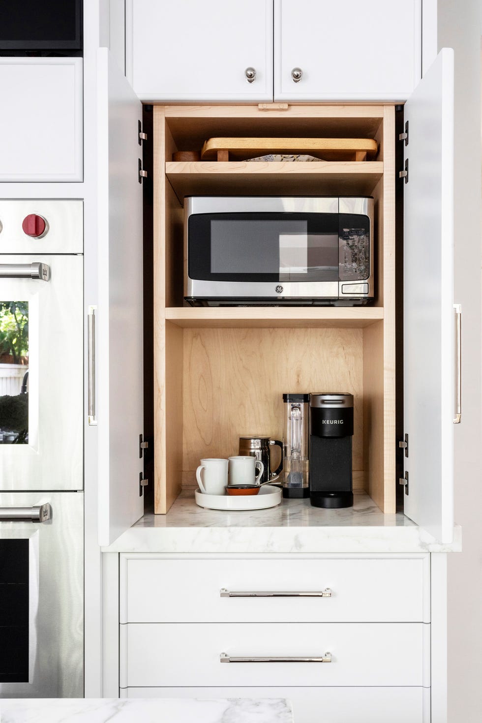 A microwave and coffee maker hidden in a cabinet in a home kitchen, designed by Andy Morse of Morse Design