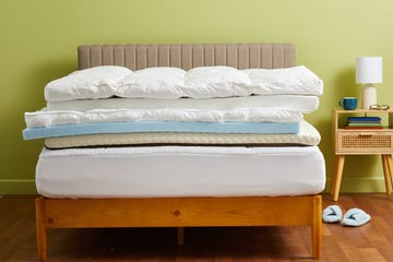 a stack of mattress toppers on a mattress in a wooden bed frame, good housekeeping's best mattress toppers