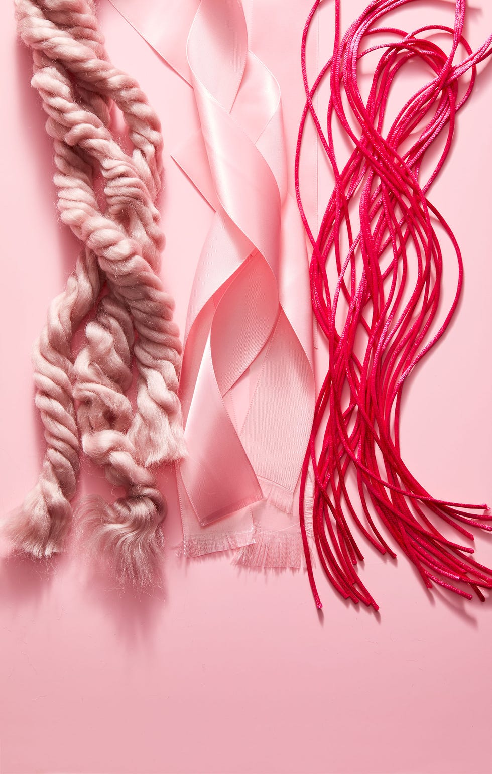 three strands of ribbon and rope with frayed ends in various shades of pink on a pink background