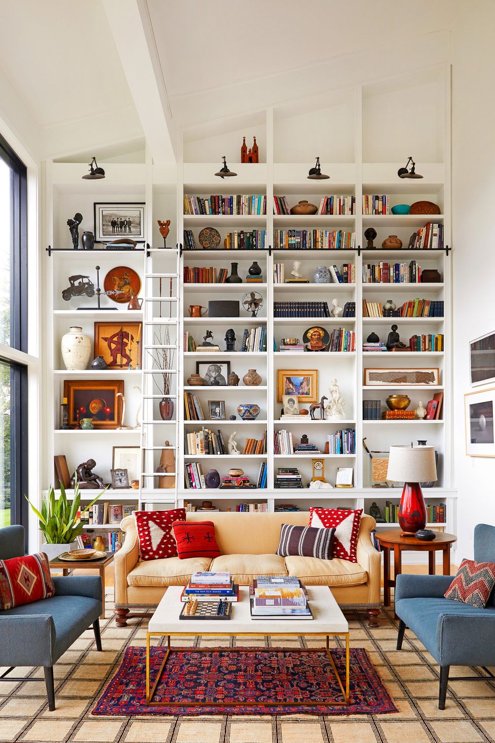 living room with high built in shelves, built ins, bookcase, white walls, ladder, storage, library