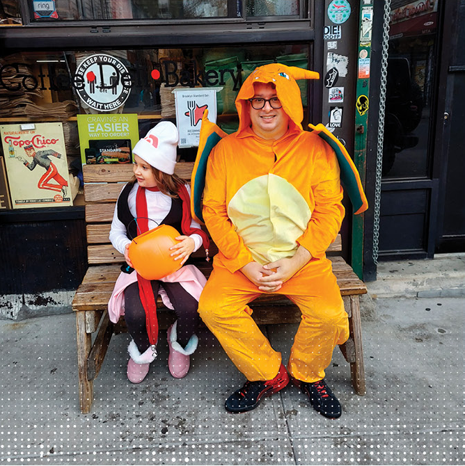 a child dressed as a pokemon trainer and a full grown man in a charizard one piece costume