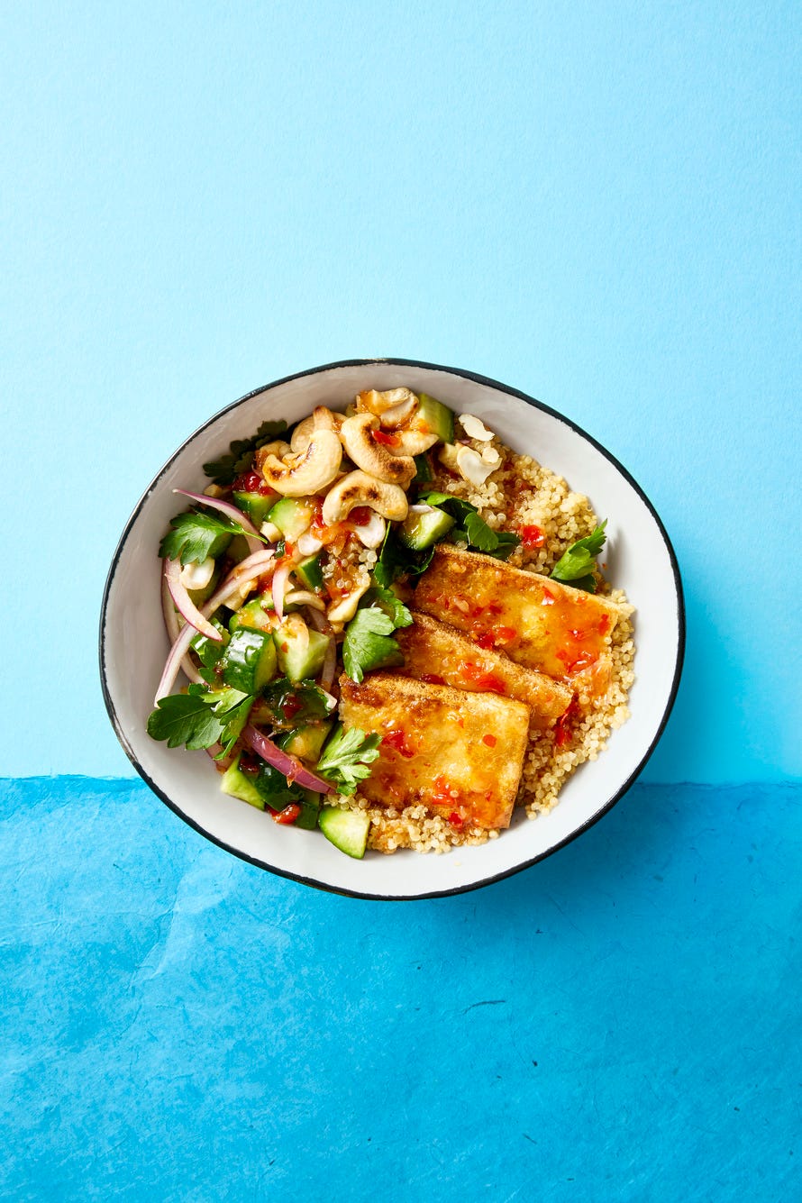a bowl of crispy tofu slices, chopped cucumber and quinoa in a white bowl