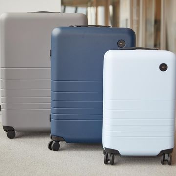three monos suitcases including a light blue carry on case, a blue medium case and a grey checked case lined up in a hallway at the good housekeeping institute