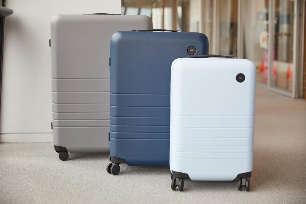three monos suitcases including a light blue carry on case, a blue medium case and a grey checked case lined up in a hallway at the good housekeeping institute