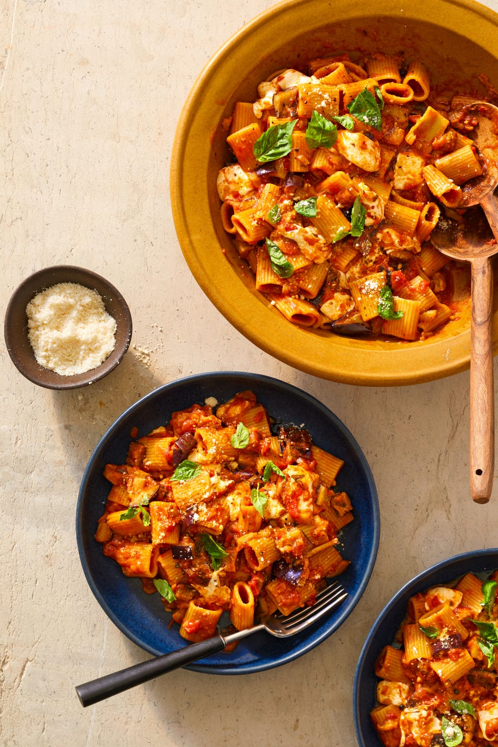 rigatoni alla norma in a serving bowl and smaller bowls with a small bowl of parmesan cheese