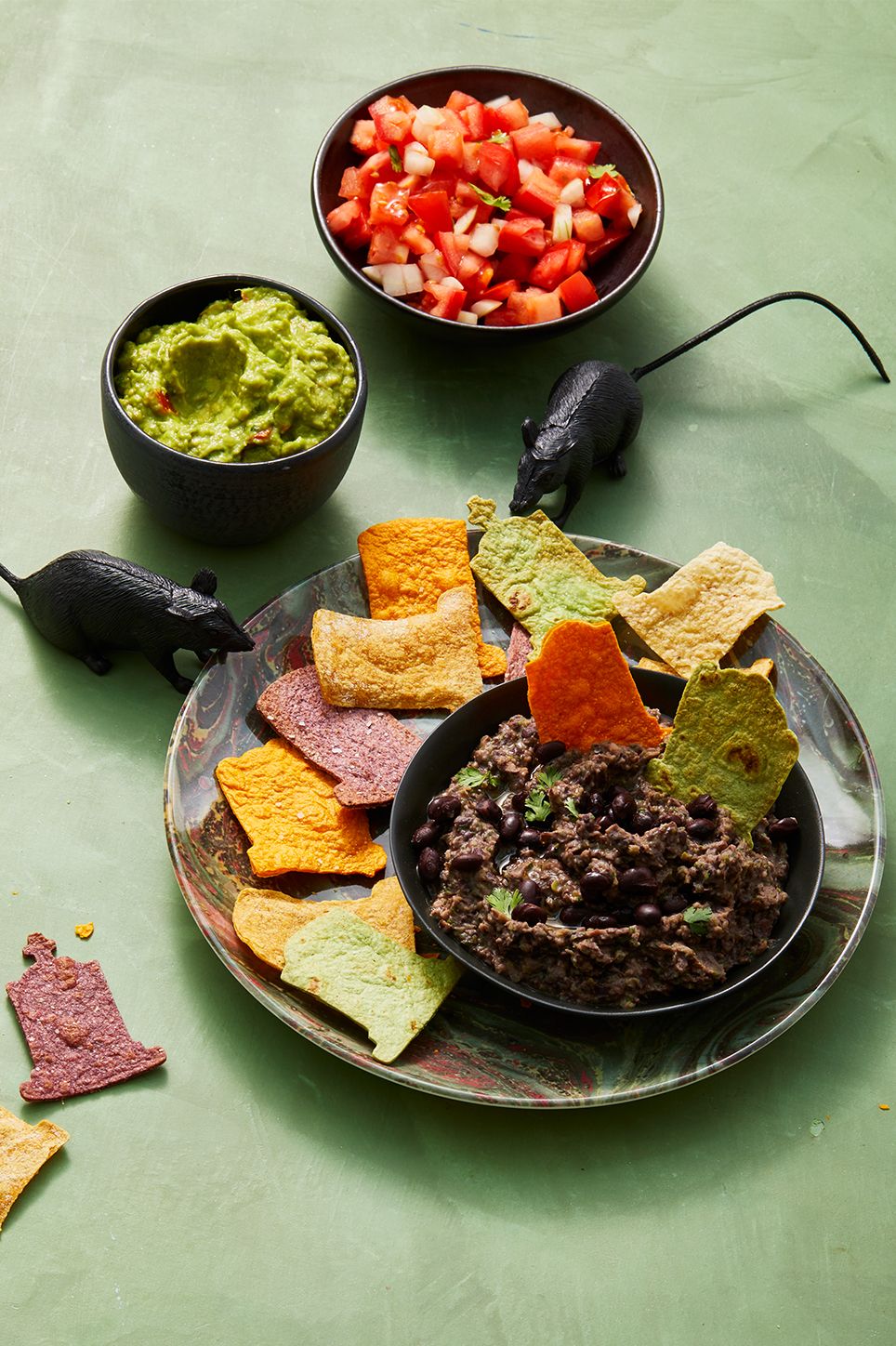 black bean dip with colorful tortilla chips and toy rats on the side