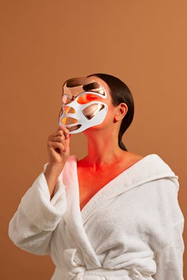 woman holding up red light mask to face