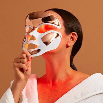 woman holding up red light mask to face