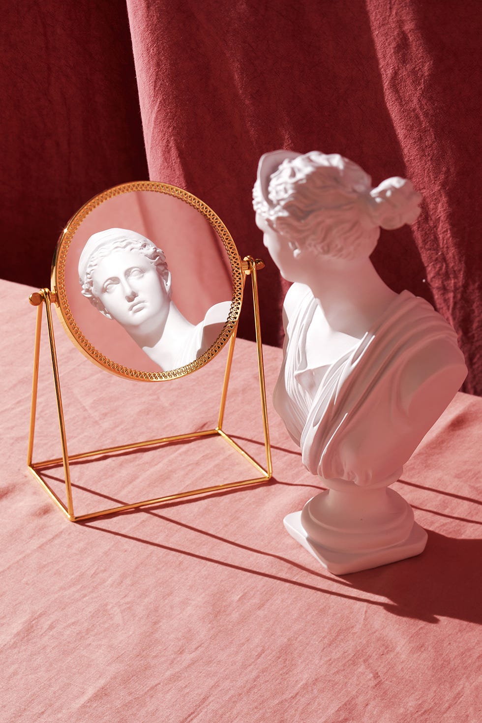 statue of bust looking into a gold mirror