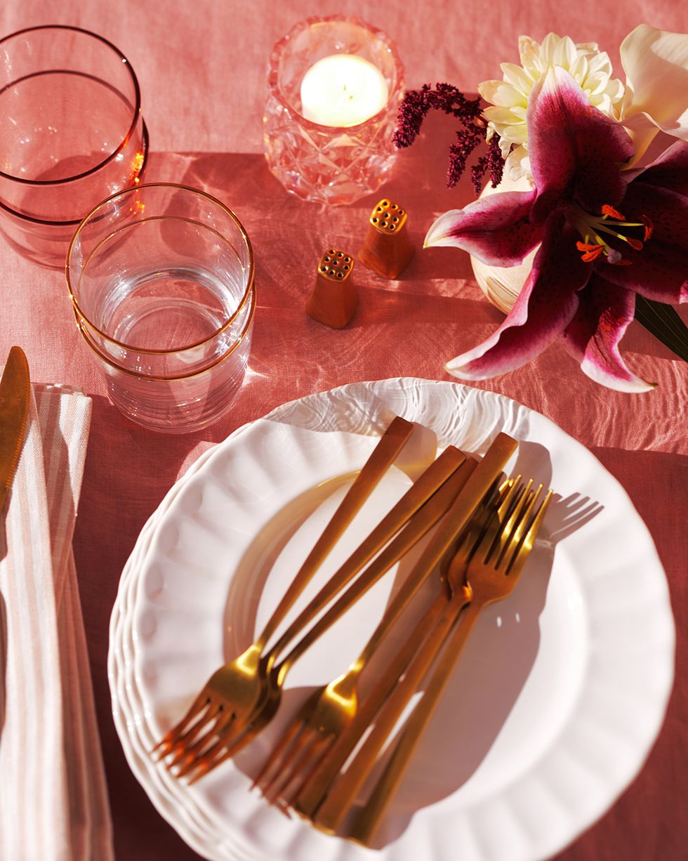 overhead shot of white scalloped plates with gold utensils on top of a pink table cloth