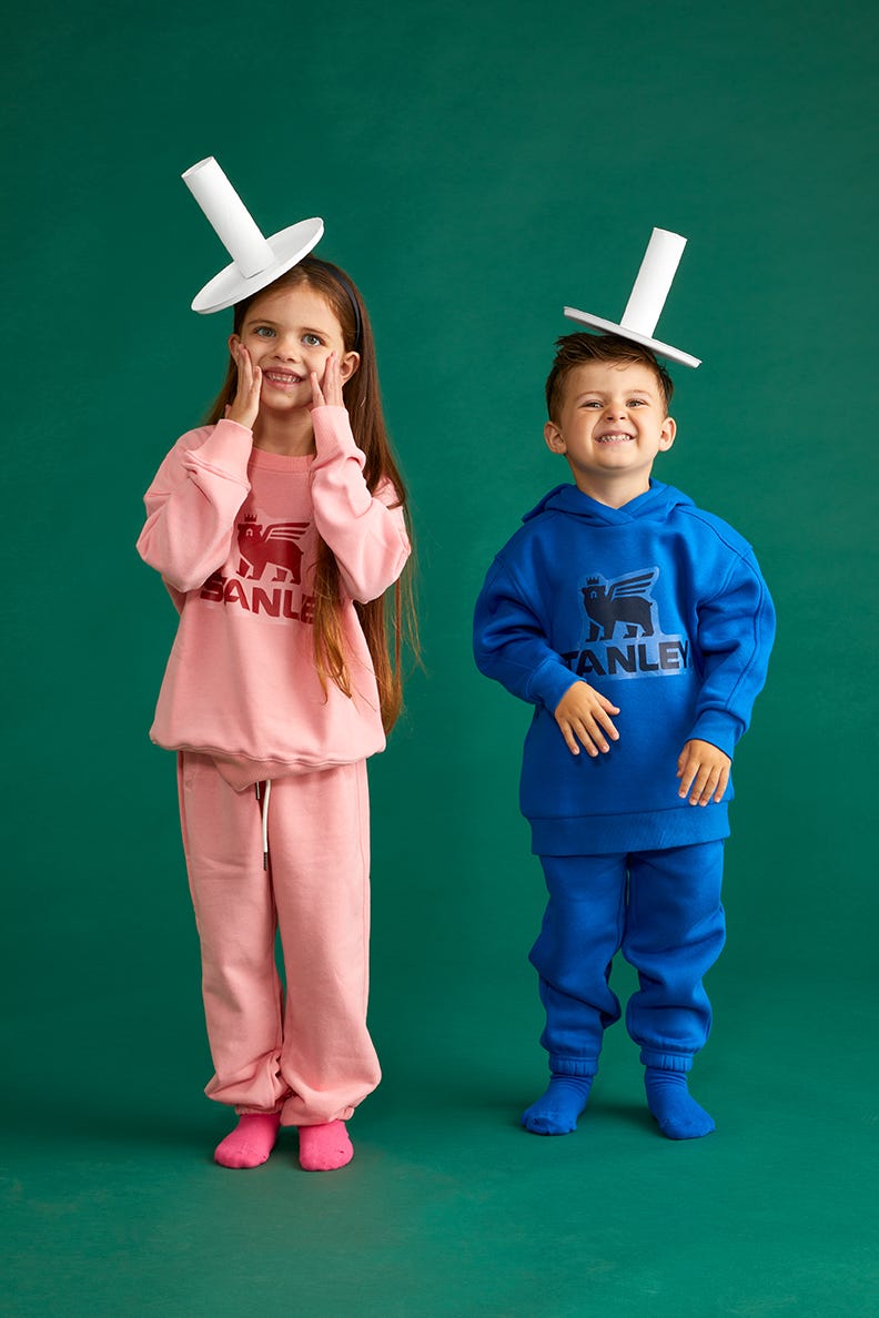 two kids dressed in sweats with the stanley logo on them and straw hats one is dressed in pink and the other in blue