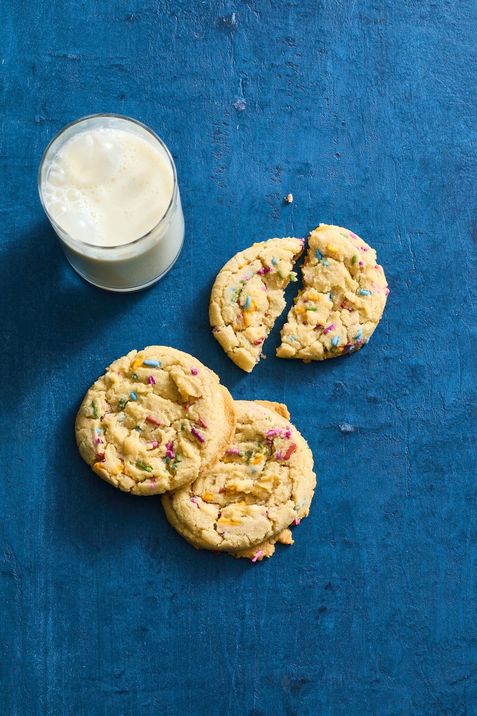 rainbow sprinkle cookies with a glass of milk on a dark blue background