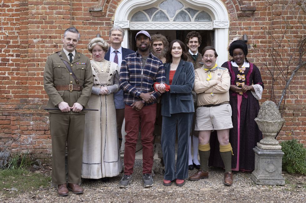 in a scene from ghosts series 5, a group of people dressed in clothes from different time periods stand outside the doorway of a stately home