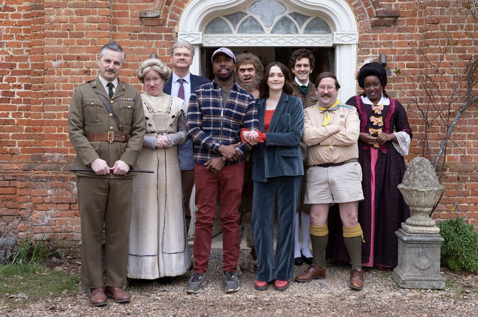 Ghosts series 5 full cast outside Button House in a scene from ghosts series 5, a group of people dressed in clothes from different time periods stand outside the doorway of a stately home