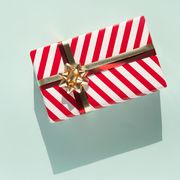 gift box with white red striped pattern and gold bow on light blue background with shadow