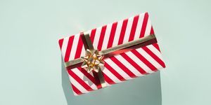 gift box with white red striped pattern and gold bow on light blue background with shadow