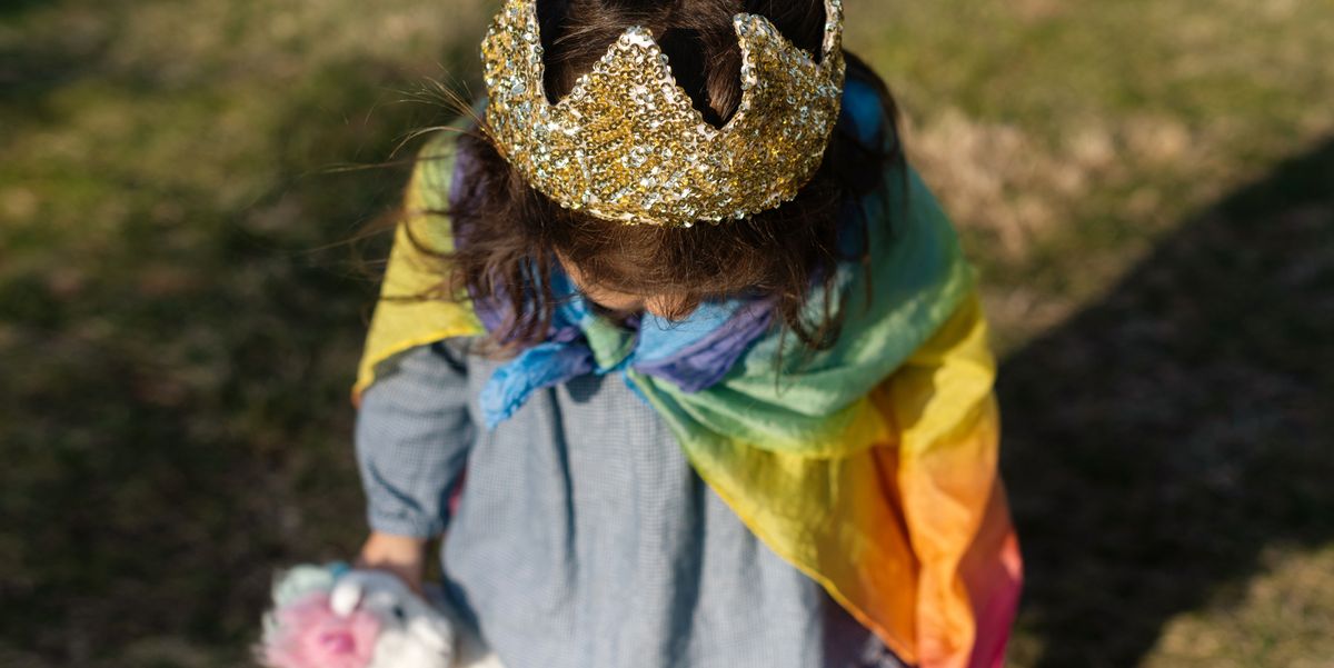 three year old girl with crown and rainbow cape on carrying unicorn toy