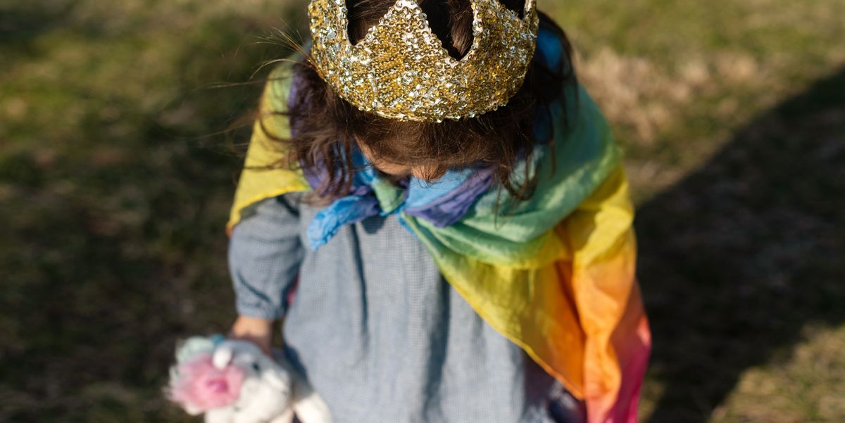 three year old girl with crown and rainbow cape on carrying unicorn toy