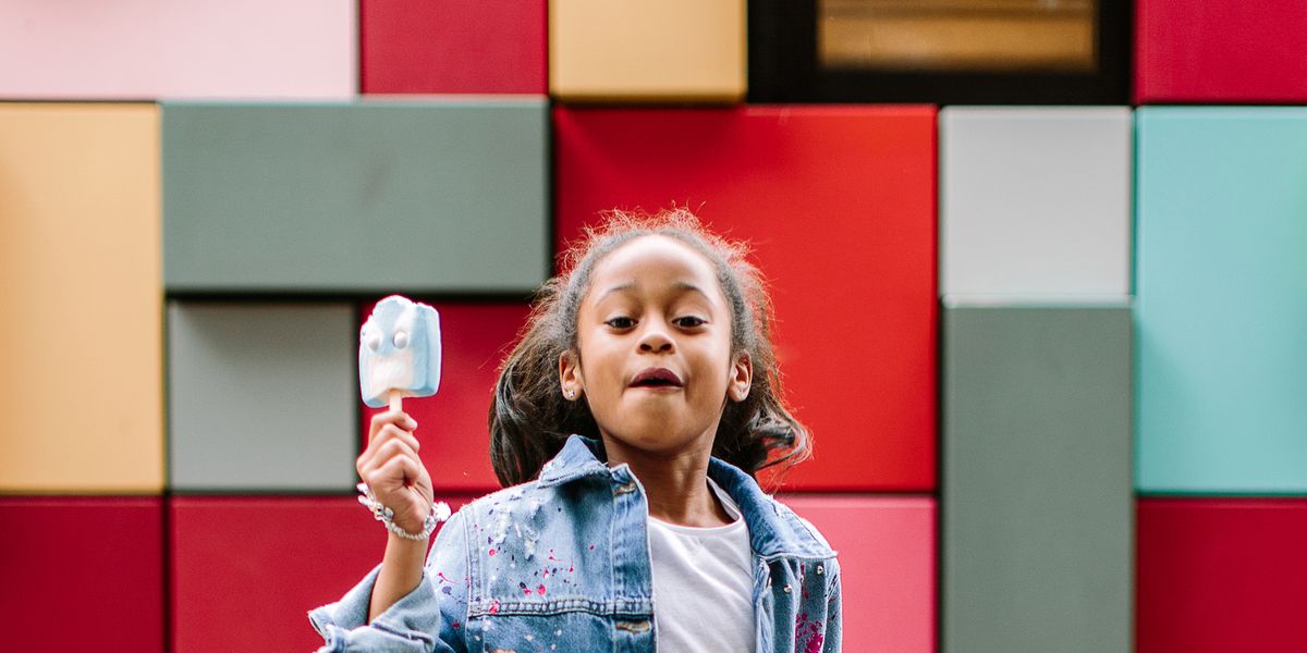 girl with popsicle jumping up against colorful tile background