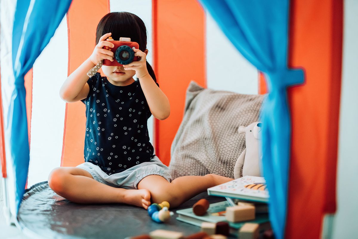 2 year old playing in play tent with camera blocks and books
