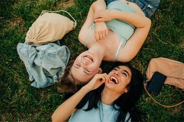 two teenage girls lying in the grass laughing together