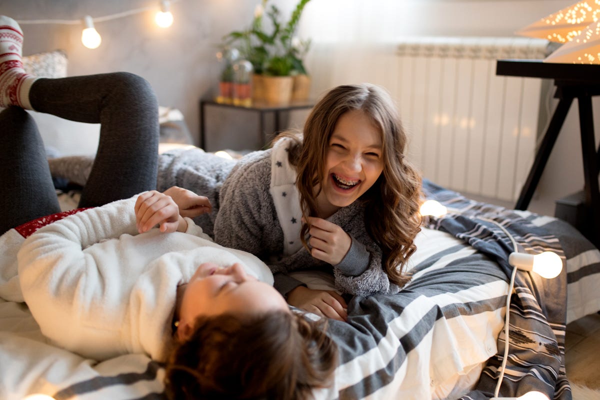 two tween girls laughing on bed with string lights