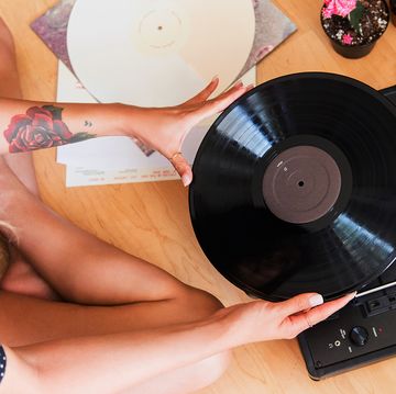woman with tattoos sitting on bedroom floor putting record on turntable
