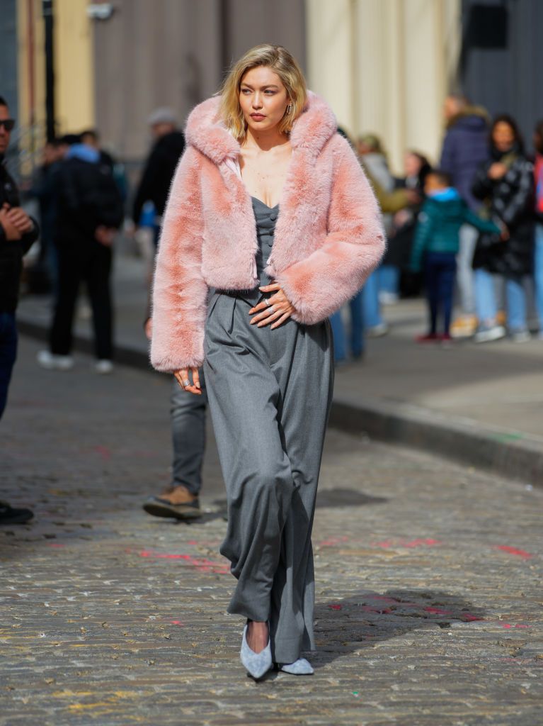 gigi hadid on set for a maybelline photoshoot in new york city wearing a grey suit and a puffy faux fur pink jacket
