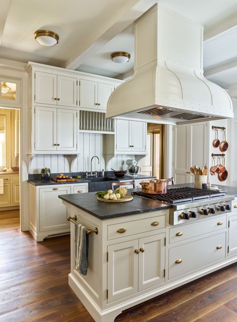 the cabinetry and custom metal hood are painted pale oak by benjamin moore and the kitchen is decorated with copper pots