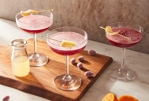 pink ginger cranberry whiskey sours in coupe glasses garnished with candied ginger
