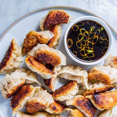 ginger pork potstickers next to a small bowl of soy sauce garnished with green onions